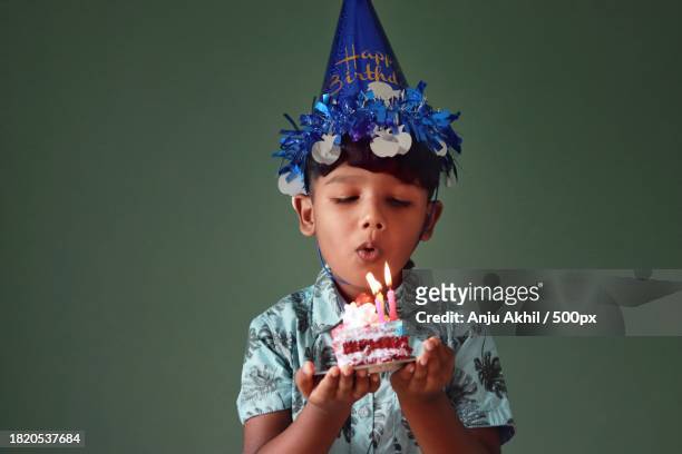 cute boy blowing party horn blower against wall,thiruvananthapuram,kerala,india - party blower stock-fotos und bilder