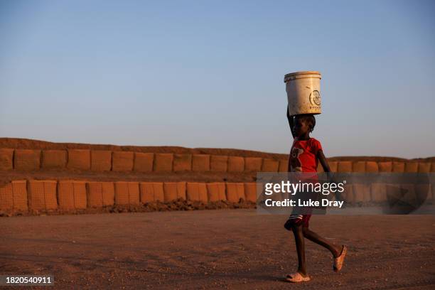 Young girl carries water along a road reclaimed from floodwater, and now protected by dykes, on November 28, 2023 in Bentiu, South Sudan. Climate...