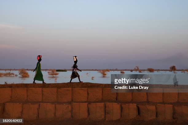 Women walk along a dyke protecting Internally Displaced Persons , and their host community, from further flooding on November 28, 2023 in Bentiu,...