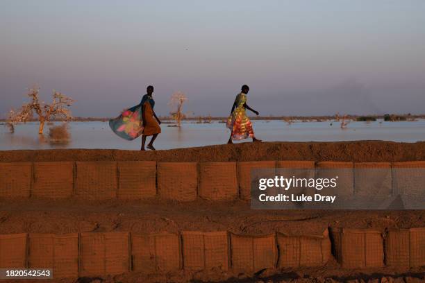 Women walk along a dyke protecting Internally Displaced Persons , and their host community, from further flooding on November 28, 2023 in Bentiu,...