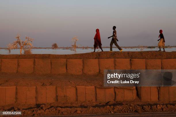 Group of people walk along a dyke protecting Internally Displaced Persons , and their host community, from further flooding on November 28, 2023 in...