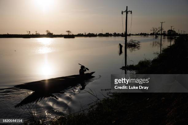 Man paddles a pirogue between partly submerged electricity pylons, and a road reclaimed from floodwater, on November 28, 2023 in Bentiu, South Sudan....