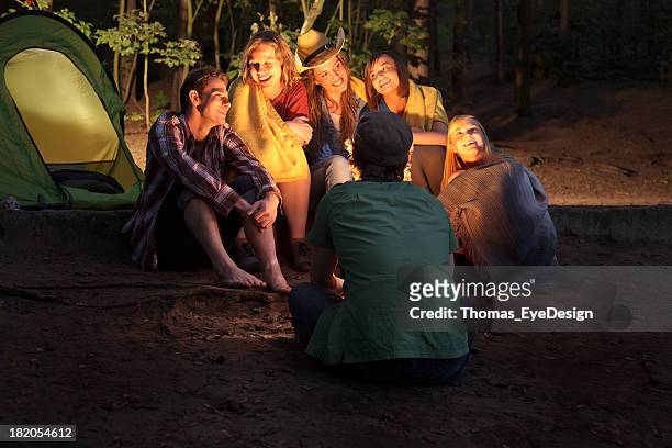 group of friends sitting around a  campfire - campfire storytelling stock pictures, royalty-free photos & images