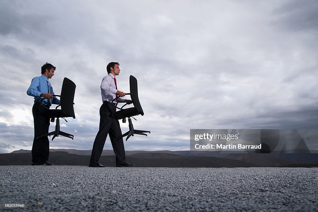 Two men carrying office chairs outdoors