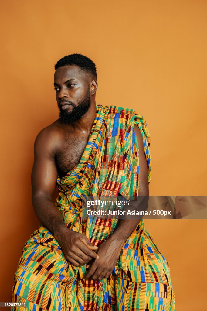 Man wearing virtual reality simulator while wearing traditional clothing against orange background,Accra,Ghana