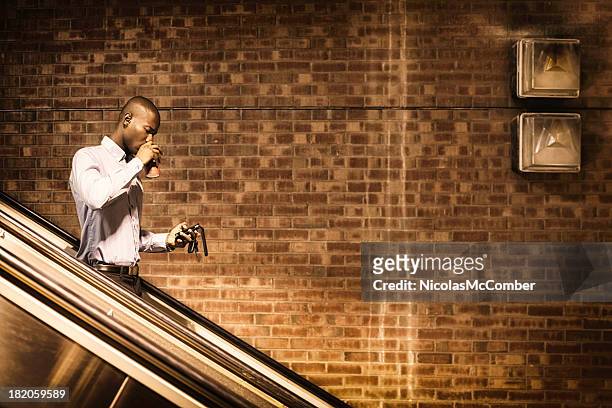 black man text messaging while commuting morning drinking coffee - escalator side view stock pictures, royalty-free photos & images