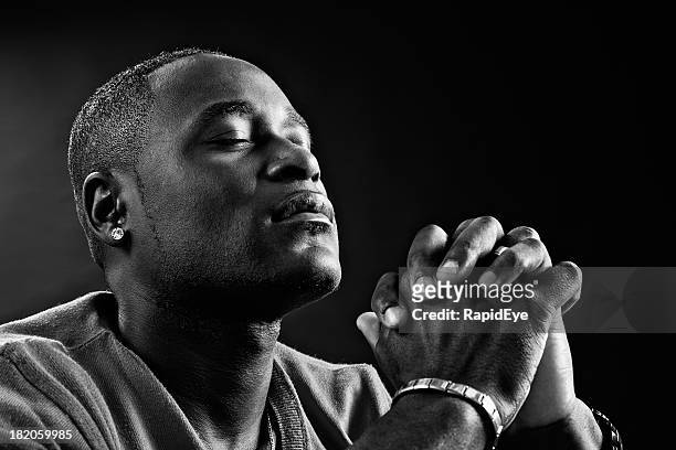 devout african-american man praying fervently in black-and-white portrait - preacher stock pictures, royalty-free photos & images