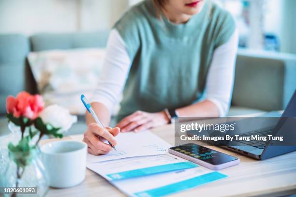 young asian women managing home finance using laptop & smartphone. she is working with household utility bill and calculating expenses at home. - tasse foto e immagini stock