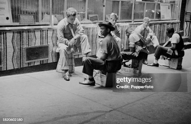 Night time view of customers having their shoes cleaned by shoeshine boys on a street off Broadway near Times Square in midtown Manhattan, New York...