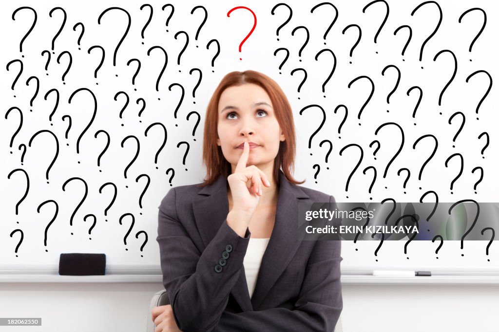 Thinking woman in front of question marks written whiteboard