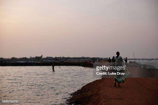 Pedestrians walk along a risen dirt road, recently reclaimed from floodwater, on November 29, 2023 in Benitu, South Sudan. Climate change has divided...