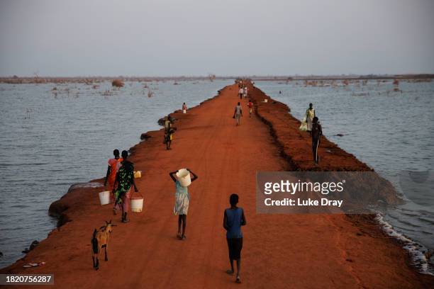 Pedestrians walk along a risen dirt road, recently reclaimed from floodwater, on November 29, 2023 in Benitu, South Sudan. Climate change has divided...