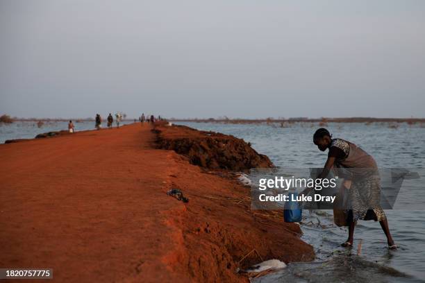 Lady collects water from the side of a road recently reclaimed from floodwater on November 29, 2023 in Benitu, South Sudan. Climate change has...