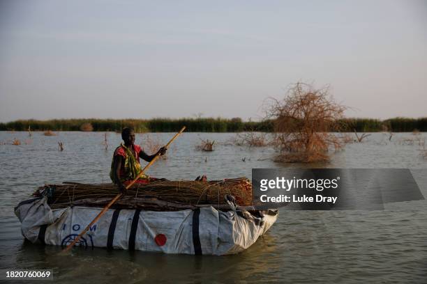 Lady paddles a raft of firewood, collected from trees killed by floodwater, to sell at the Internally Displaced Persons camp on November 29, 2023 in...