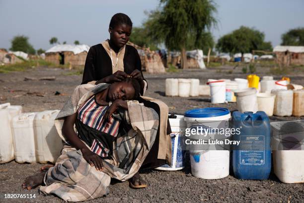 Young girl braids another's hair at a water pumping station in an Internally Displaced Persons camp on November 29, 2023 in Rotriak, South Sudan....