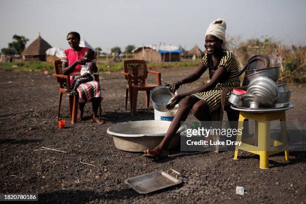Lady interacts with her friends whilst washing dishes at an Internally Displaced Persons camp on November 29, 2023 in Rotriak, South Sudan. Climate...