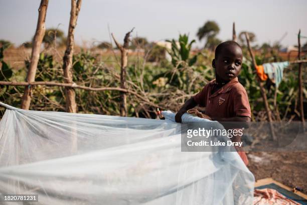 Young boy rolls up a mosquito net covering bedding at an Internally Displaced Persons camp on November 29, 2023 in Rotriak, South Sudan. Climate...