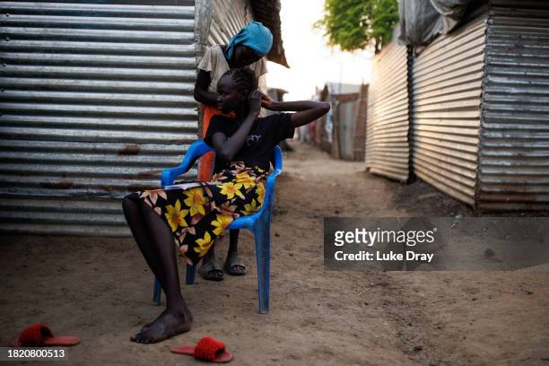 Young woman does her homework as her hair is braided by a friend in an Internally Displaced Persons camp on November 29, 2023 in Bentiu, South Sudan....