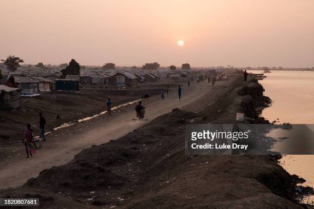People walk past a dyke protecting Internally Displaced Persons , and their host community, from further flooding on November 29, 2023 in Bentiu,...