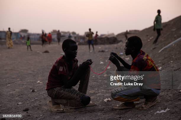 Two young boys bead a necklace in an Internally Displaced Persons camp on November 29, 2023 in Bentiu, South Sudan. Climate change has divided South...