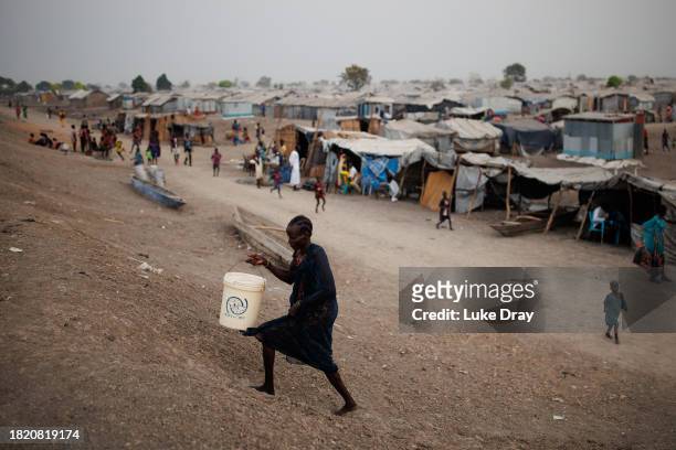 Woman fetches water from over a dyke protecting Internally Displaced Persons , and their host community, from further flooding on November 29, 2023...