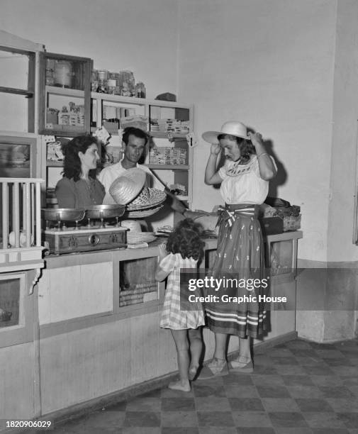 Swedish actress Ingrid Bergman buying a straw hat in a general store, Stromboli, Italy, 1950. Bergman is on the island to film 'Stromboli', with...