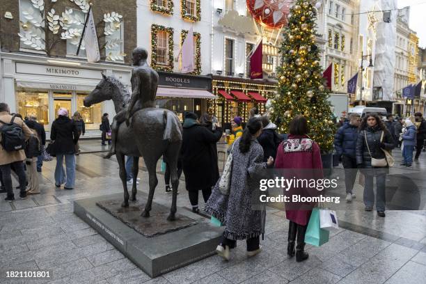 Shoppers pass a statue and Christmas tree on Bond Street in London, UK, on Monday, Dec. 4, 2023. Inflation in UK shops has fallen to a 17-month low...