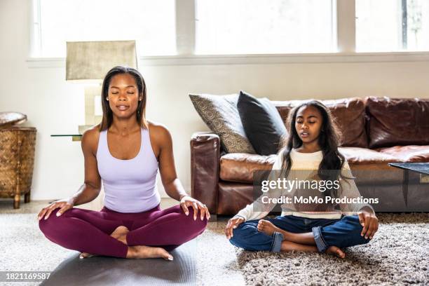 mother and daughter meditating in living room - rolled up yoga mat stock pictures, royalty-free photos & images