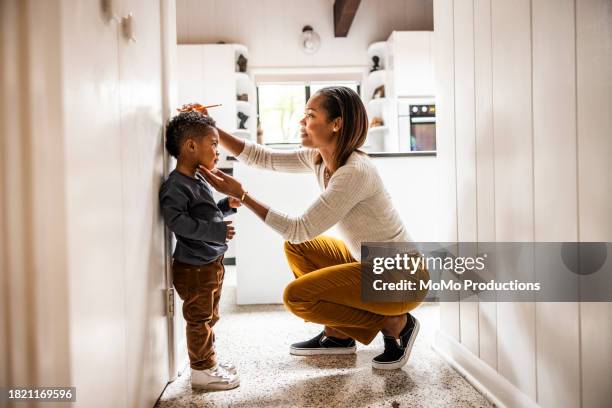mother measuring son's height on wall in kitchen - lang lichaamslengte stockfoto's en -beelden