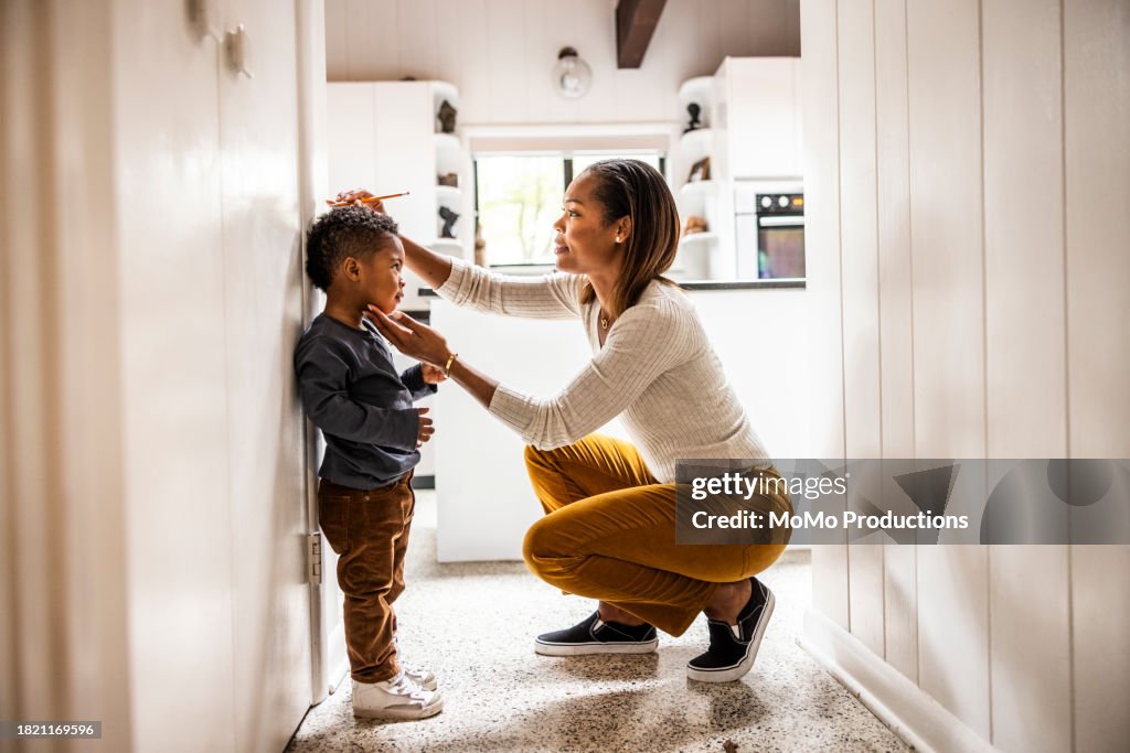 Mother measuring son's height on wall in kitchen
