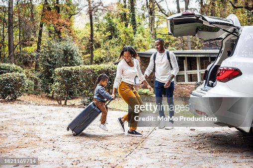 Mother pulling young boy on suitcase and loading car for family vacation Mother pulling young boy on suitcase and loading car for family vacation