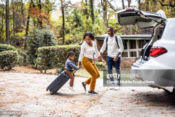 mother pulling young boy on suitcase and loading car for family vacation - family travel stock pictures, royalty-free photos & images