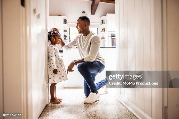 father measuring daughter's height on wall in kitchen - estatura humana fotografías e imágenes de stock