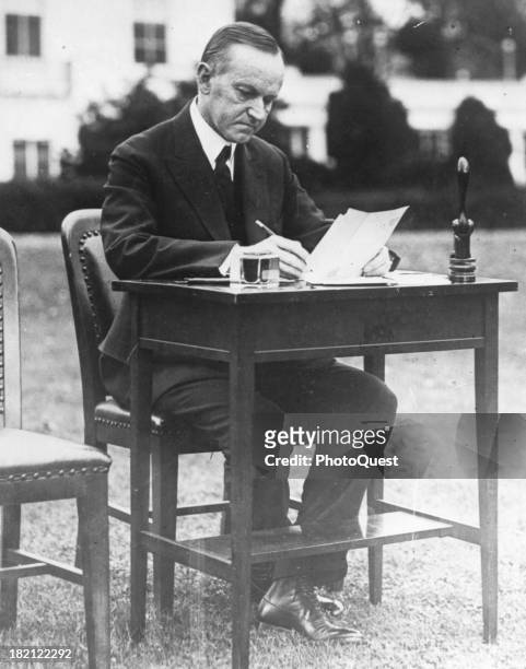 American poltician US President Calvin Coolidge sits at a writing desk on the White House lawn as casts his absentee ballot for the 1924 general...