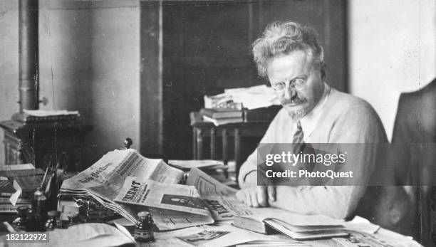 Russian revolutionary and political theorist Leon Trotsky poses at his desk, an open newspaper in front of him, early to mid 20th century.