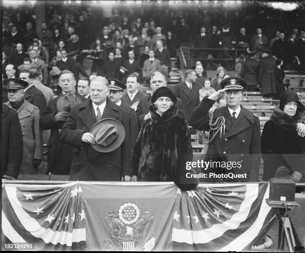 With unidentified others, American politician US President Herbert Hoover and his wife, First Lady Lou Henry Hoover , stand at attention on a...