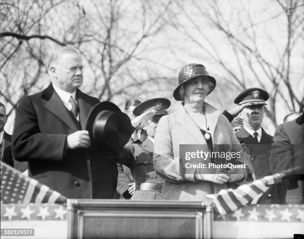 American politician US President Herbert Hoover and his wife, First Lady Lou Henry Hoover , stand at attention on a reviewing stand, March or April...