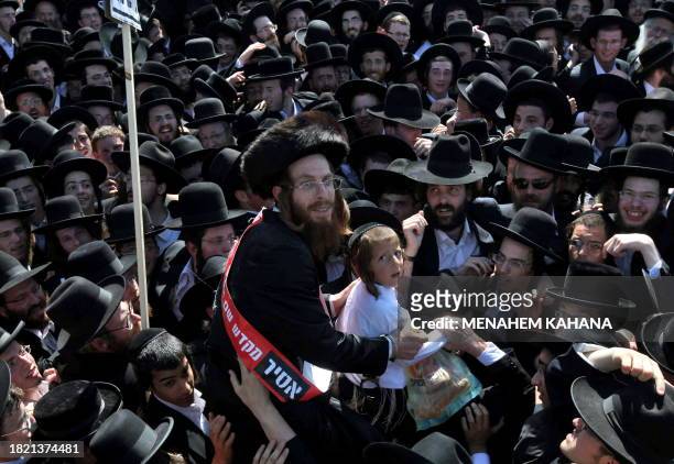 An Ultra-Orthodox Jewish man who is supposed to go to jail, is carried by the crowd with his son while wearing a banner that reads "prisoner in the...