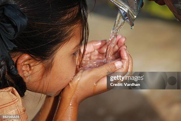 small dark haired child drinking water using her hands - faucet stockfoto's en -beelden