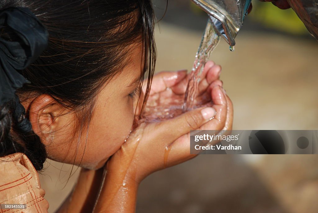 Small dark haired child drinking water using her hands