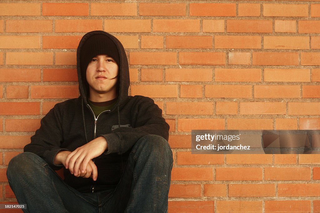 Teenage boy dressed in black crouched down on brick wall 