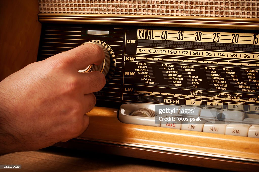 Vintage short wave radio with person's hand on the tuner