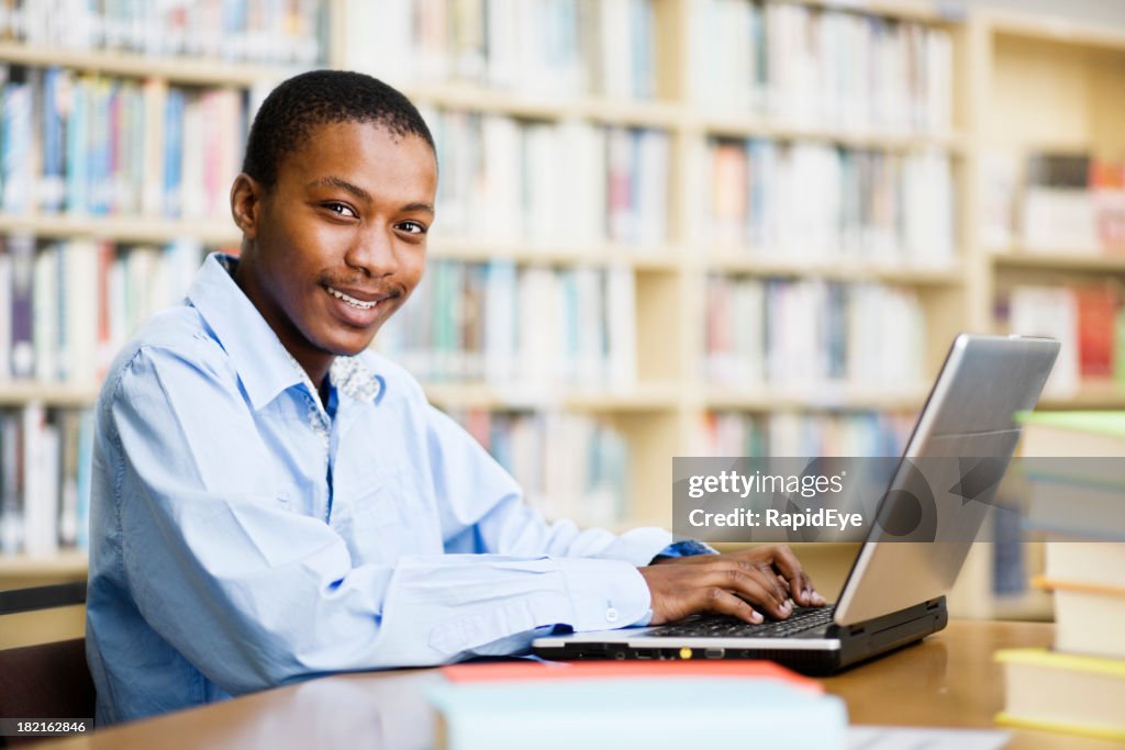 Happy student in library smiles up from his laptop