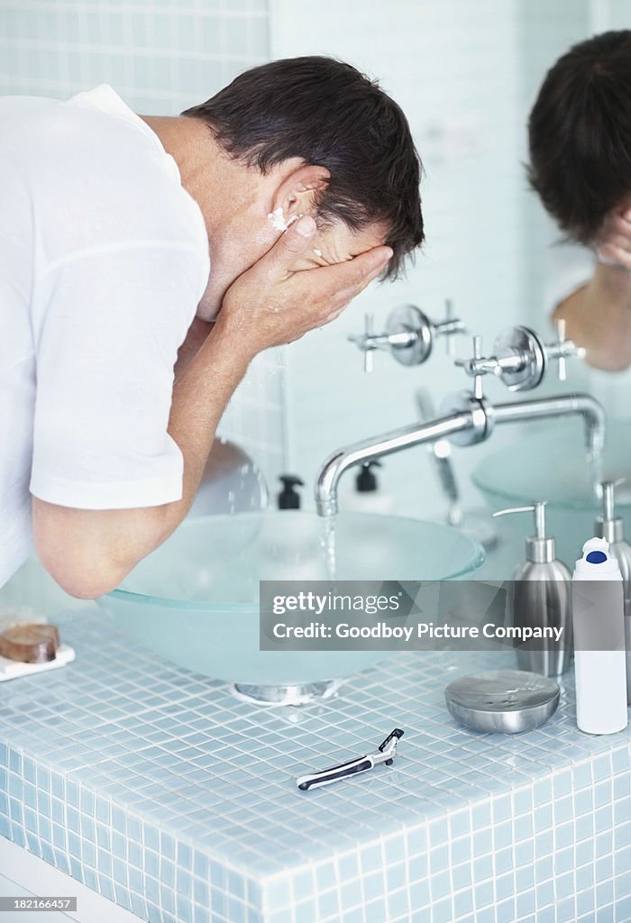 Man rinsing shaving cream off his face in bathroom