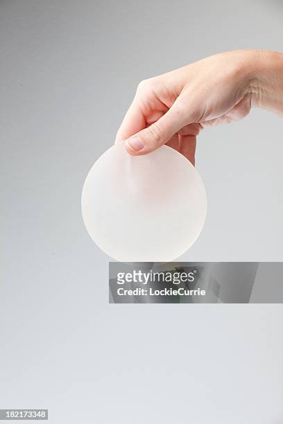 a hand holding a silicone breast implant - silikone stock pictures, royalty-free photos & images