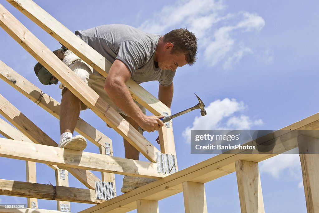 Builder Hammering Roof Truss Nail Against Blue Sky