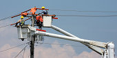 Two workers in a crane repairing a power pole