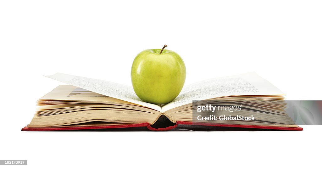 Green apple on a red book, isolated