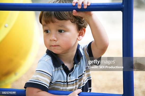 concerned young boy holding on to bar at a playground - nursery school child stock pictures, royalty-free photos & images