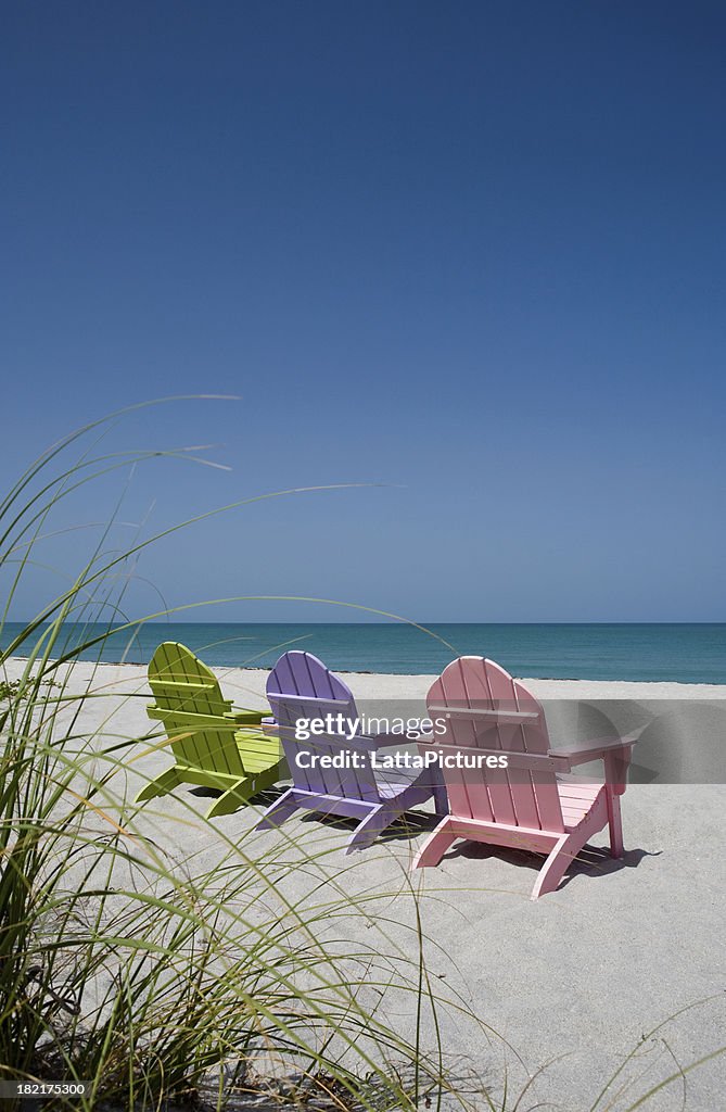 Back view of three pastel colored beach chairs on sand